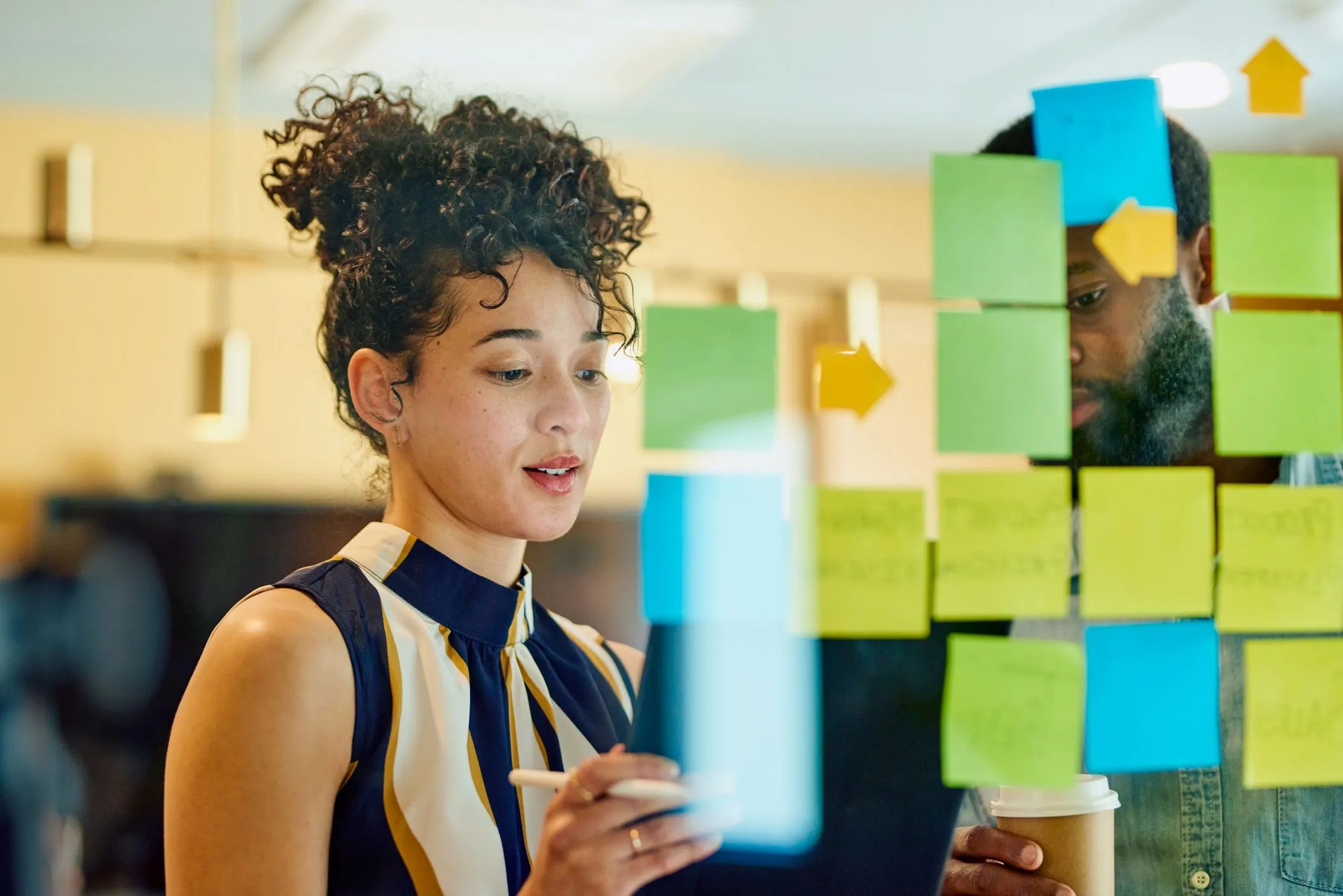 Two colleagues brainstorming ideas with sticky notes on a glass board