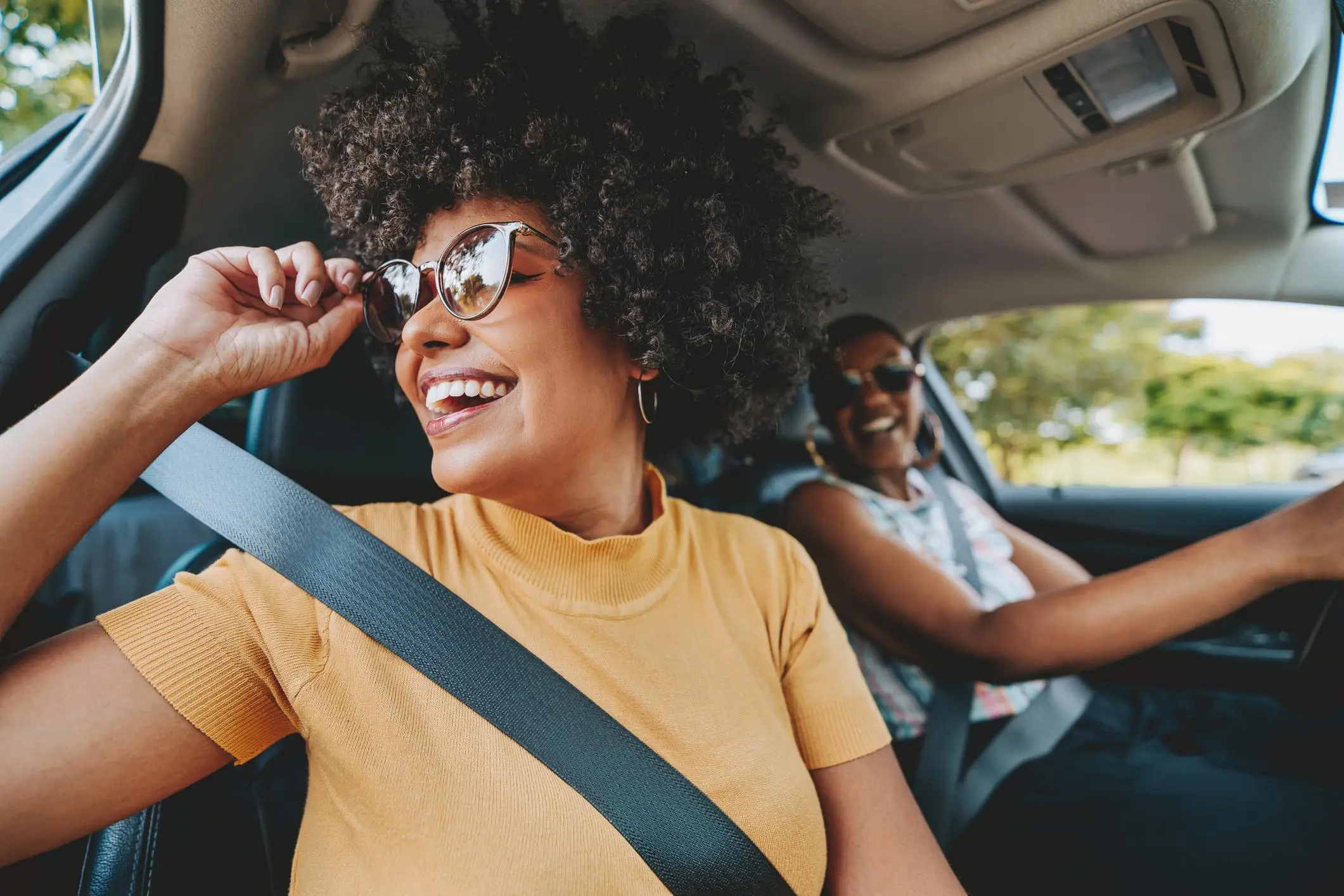 Two women enjoying a car ride, smiling and wearing sunglasses, representing the freedom that can come from a financial checkup.