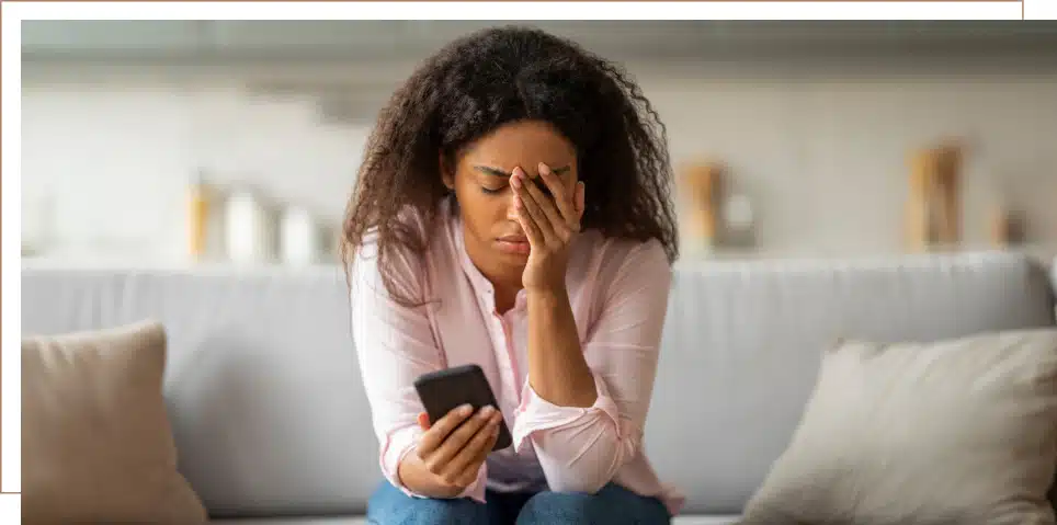 A frustrated woman holds a cell phone in one hand and her face in the other.