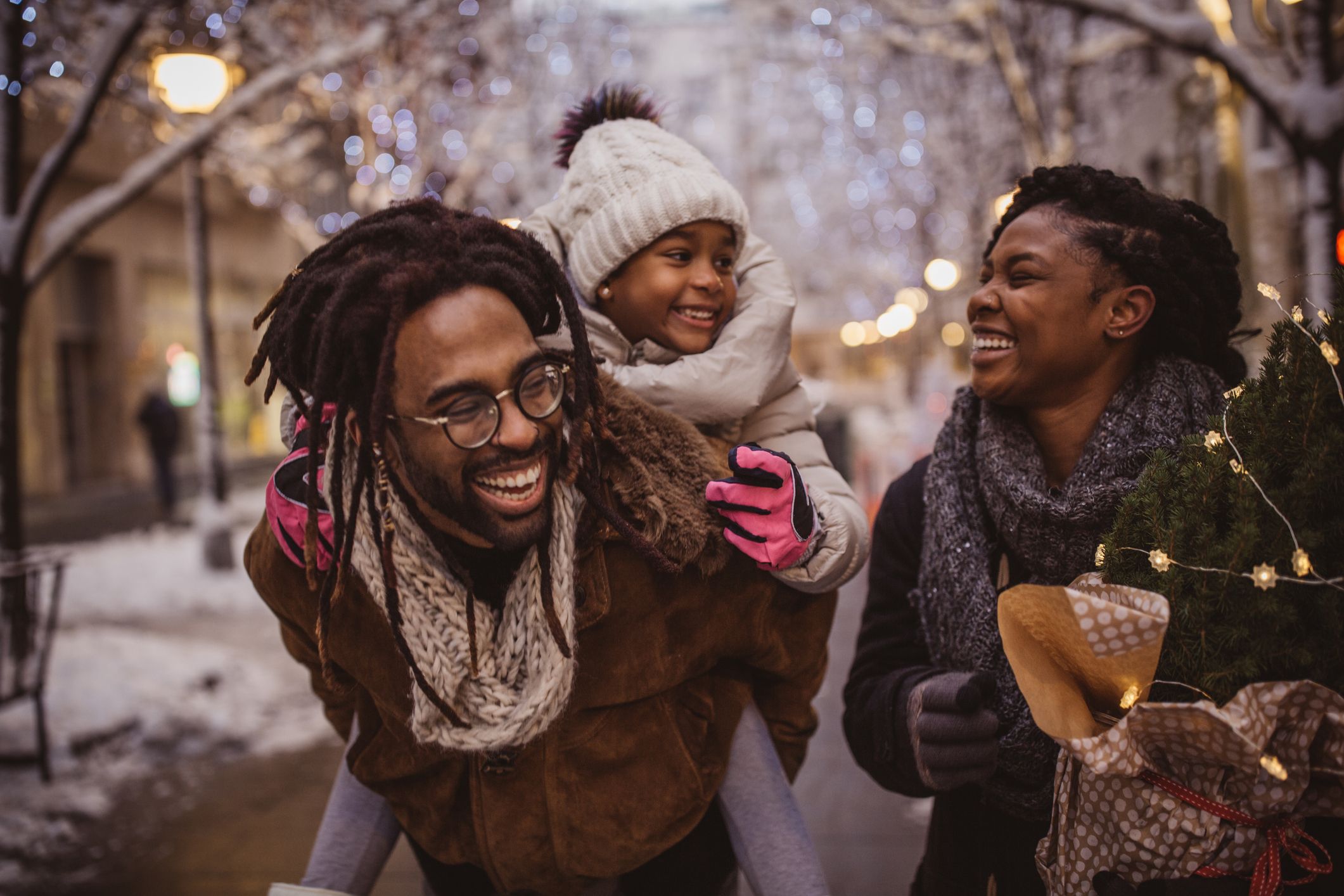 A young family preparing for the holiday. They're walking on the street and carrying Christmas stuff